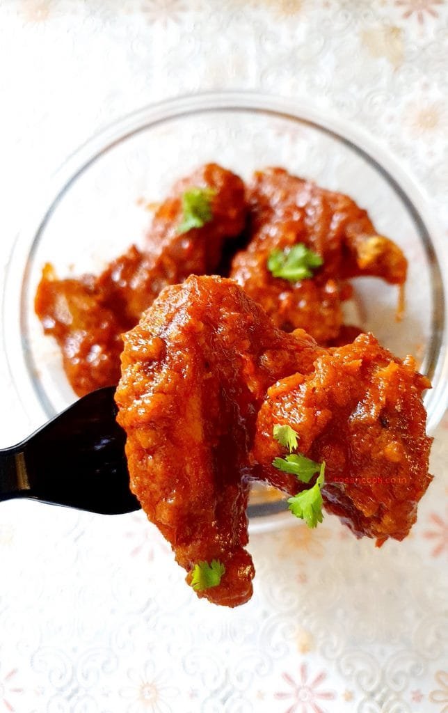 A piece of chicken wings red in color and sprinkled with coriander held on a spoon