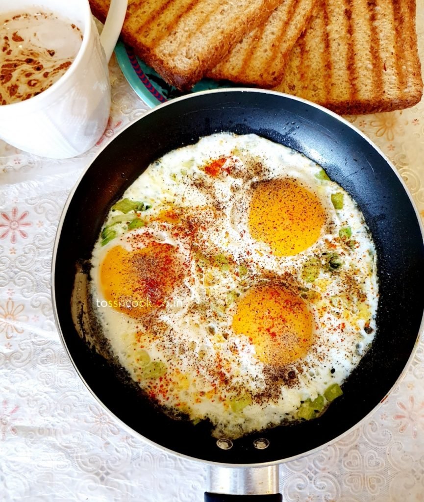 Masala Fried Eggs in a round pan with coffee and bread toast in the side