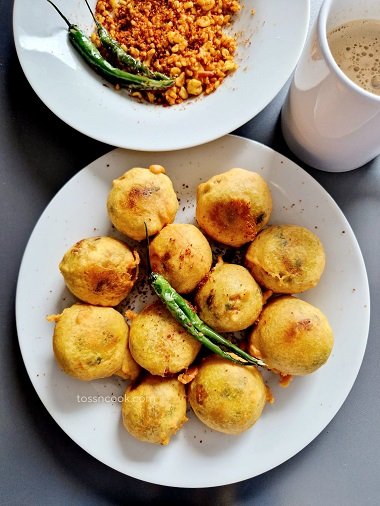 Batata Vada served in a plate with green chilli on top and chutney and coffee in the side