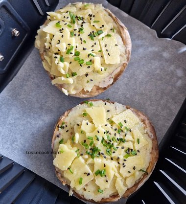 Raw Stuffed Mushrooms placed in the air fryer. Stuffed with fillings and cheese on top sprinkled with nigella seeds and parsley